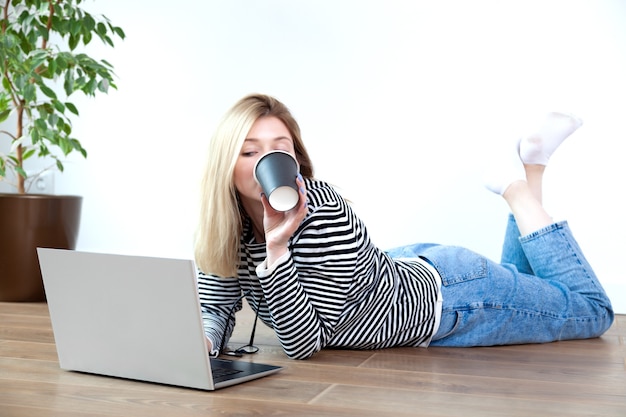 Blonde young woman drinking coffee from black paper cup