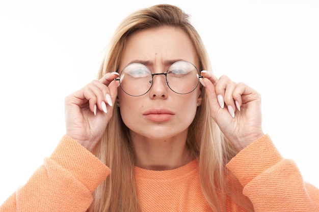 Blonde young woman wearing glasses squinting while looking at camera isolated on white background Vision problems concept