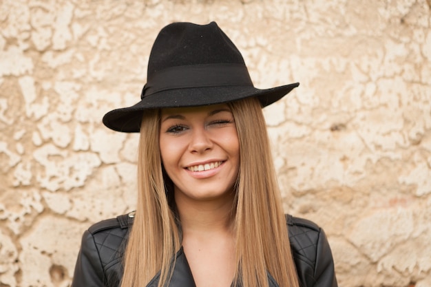 Blonde young woman with black hat winking a eye