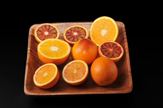 Blood oranges whole and cut in half on a wooden bowl