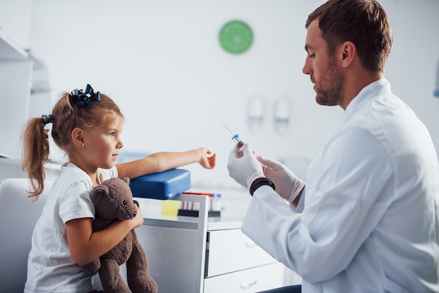 Blood sampling. Little girl with her teddy bear is in the clinic with doctor.