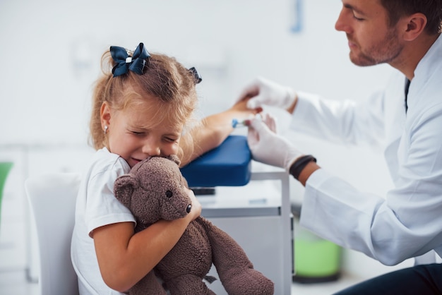 Blood sampling. Little girl with her teddy bear is in the clinic with doctor.