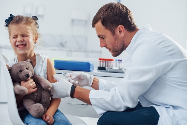 Blood sampling. Little girl with her teddy bear is in the clinic with doctor.