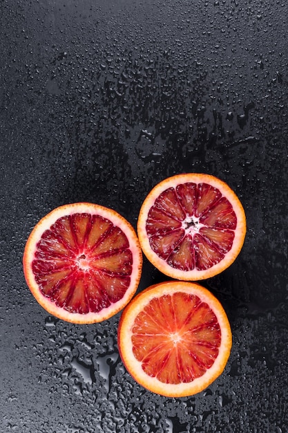 Photo bloody oranges cut in half on black slate board with water drops, red sicilian orange fruit, top view, free space for text.