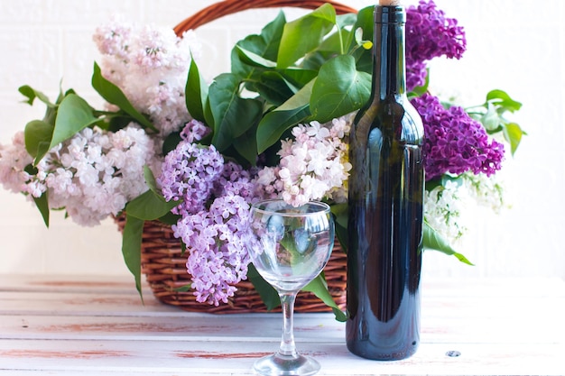 A blooming bouquet of lilacs in a wicker basket A bottle of wine and a glass glass