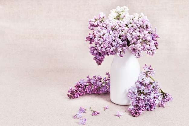 Blooming Lilac flowers in white vase on rustic 