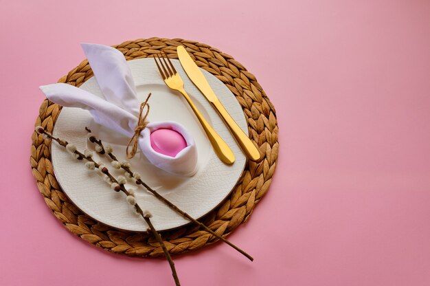 Blooming willow branch, easter egg on plate and tableware on pink background