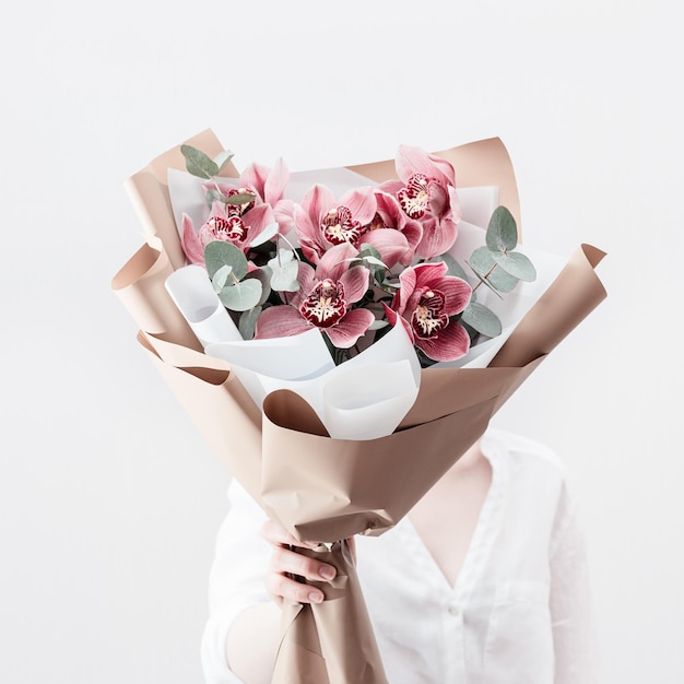 Blossoming delicate flowers of pink orchid in hands of female on light background Modern bouquet