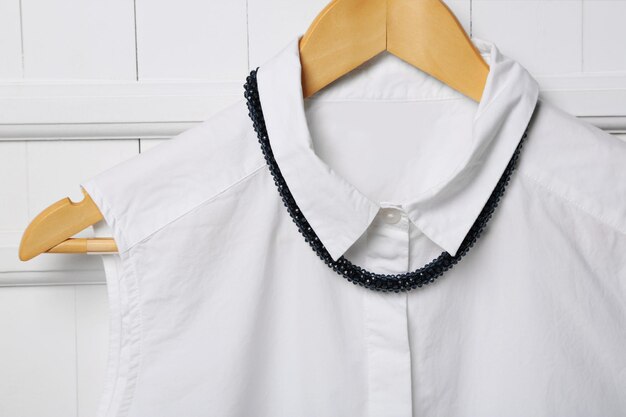 Blouse and necklace on hanger on wall background