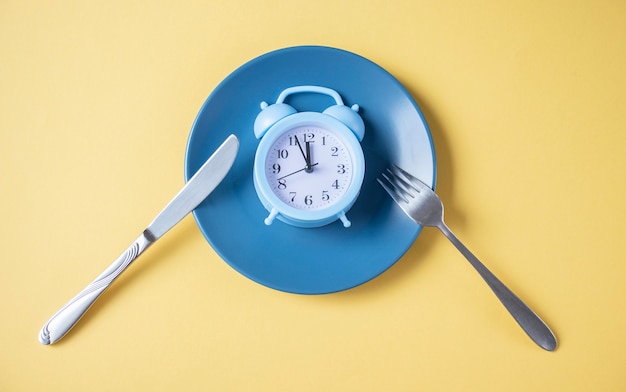 Blue alarm clock on an empty blue plate on a yellow