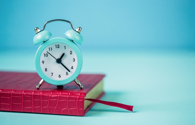 Blue alarm clock, red notepad on a blue background. The concept of time planning. Close-up. Empty space for the text.