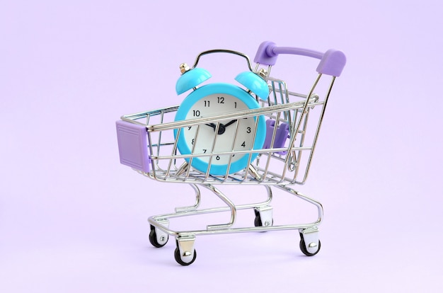 Blue alarm clock in supermarket trolley on violet background