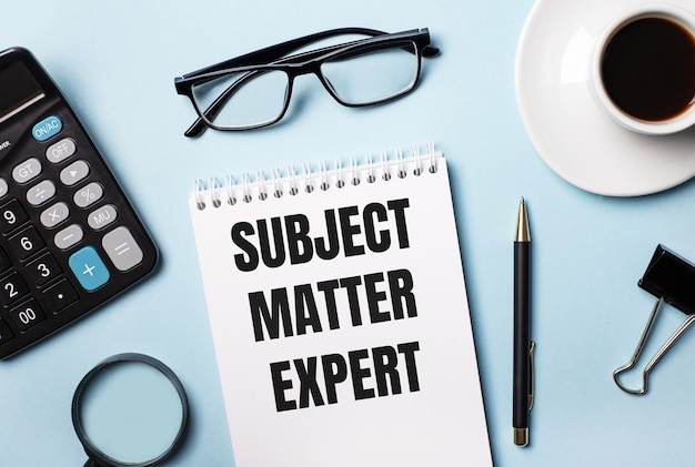 On a blue background, glasses, calculator, coffee, magnifier, pen and notebook with the text SUBJECT MATTER EXPERT