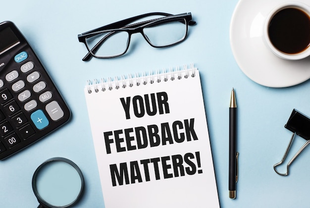 On a blue background, glasses, calculator, coffee, magnifier, pen and notebook with the text YOUR FEEDBACK MATTERS