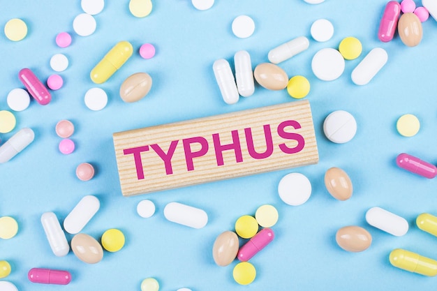 On a blue background multicolored pills and a wooden block with the text TYPHUS View from above Medical concept