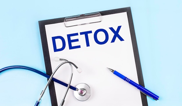 On a blue background a stethoscope a pen and a tablet with paper and the text DETOX Medical concept