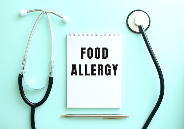 On a blue background, a stethoscope and a white notepad with the words FOOD ALLERGY