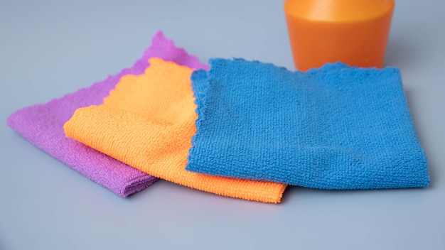 On a blue background there are microfiber cleaning cloths of different colors laid out on the back of an orange pulevizer