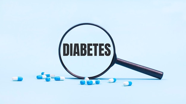 On a blue background white and blue capsules with pills and a black magnifying glass with the text DIABETES Medical concept