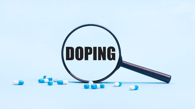 On a blue background white and blue capsules with pills and a black magnifying glass with the text DOPING Medical concept