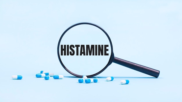 On a blue background white and blue capsules with pills and a black magnifying glass with the text HISTAMINE Medical concept