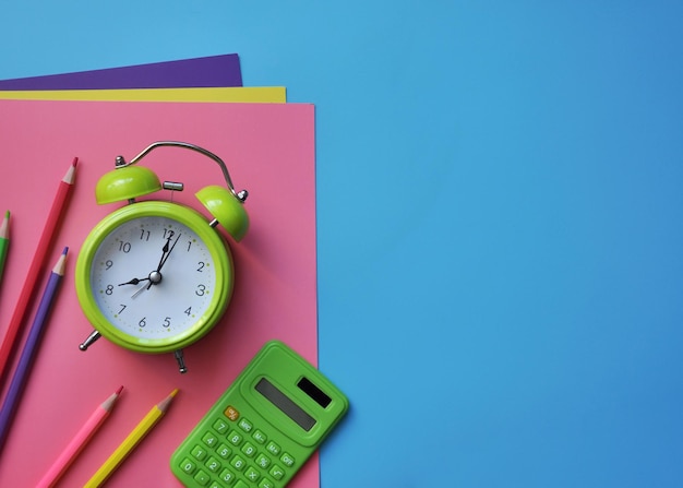 Blue background with school supplies, paper, pencils, alarm clock, calculator