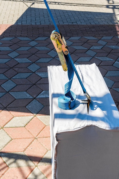 A blue belt with a tensioning device is attached to the concrete block. Cargo ties