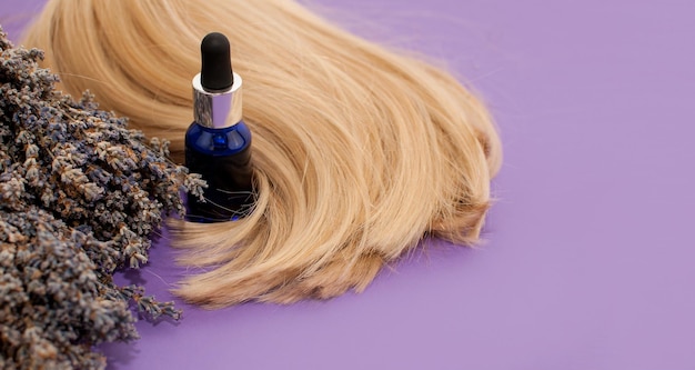 A blue bottle of oil bouquets of dried lavender and blonde hair on a purple background in the form of a banner