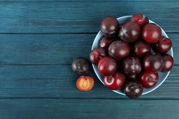 Blue bowl with plums on a blue wooden table.