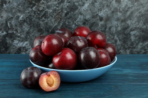 Blue bowl with plums on a blue wooden table.