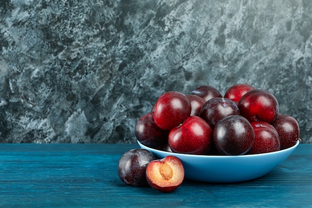 Blue bowl with plums on a blue wooden table.