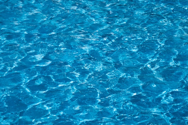 Blue and bright ripple water surface in swimming pool with sun reflection.