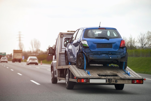 A blue car on a trailer is being towed by a tow truck.