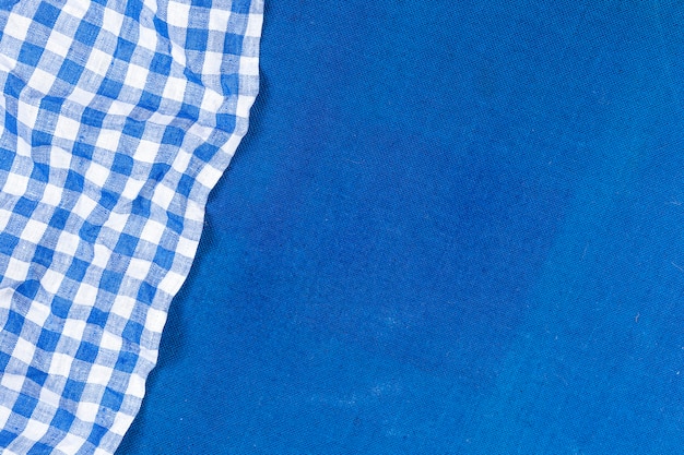 Blue checkered napkin on blue cloth background, top view