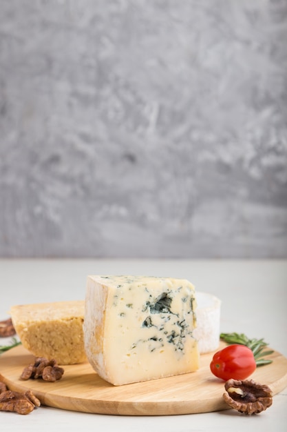 Blue cheese and various types of cheese on wooden board on a white and gray background