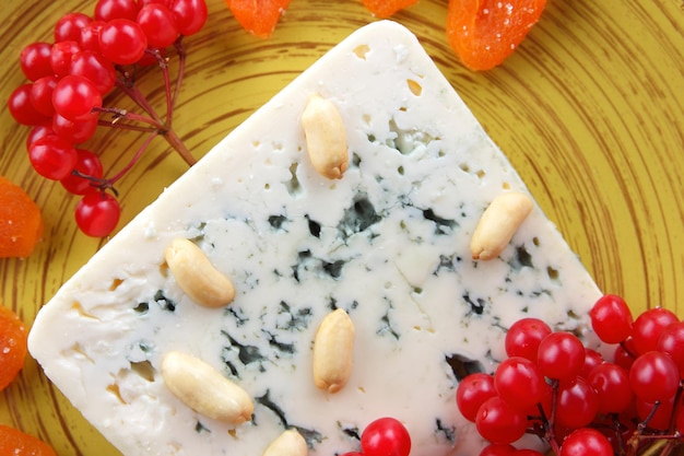 Blue cheese with nuts berries and dried fruits on a yellow plate Cheese on a blue background Closeup View from above