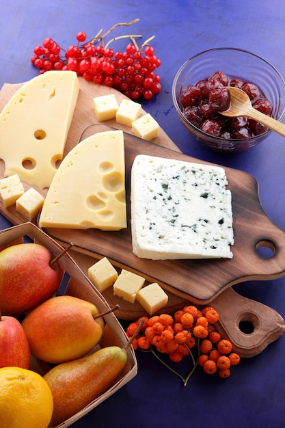 Blue cheese and yellow hard cheese with fruits and berries on wooden boards Various types of cheese composition with honey and apples in a wooden basket on a blue background