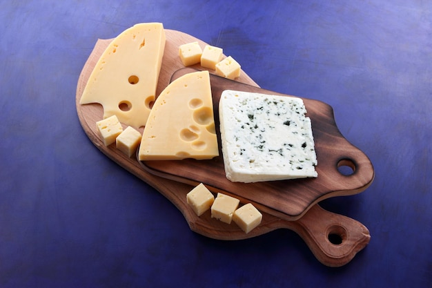 Blue cheese and yellow hard cheese on wooden boards on a blue background Various types of cheese composition closeup