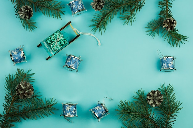 Blue Christmas background with spruce branches and cones, Christmas toys for decor, sleds with a gift, traditional Christmas drums. top view.