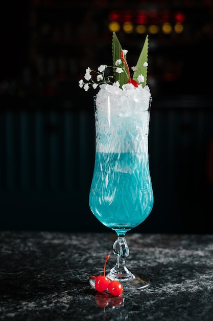 Blue cocktail garnished with cherries leaves and ice crush