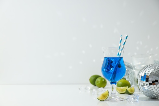 Blue cocktail in glass limes ice cubes and disco balls on white background space for text