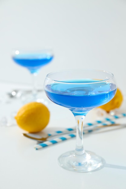 Blue cocktail in glass whole lemon straws and ice cubes on white background