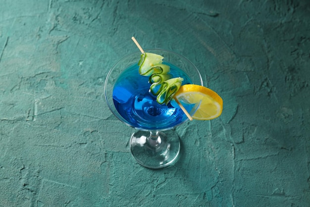 Blue cocktail with lemon and cucumber slices in glass on green background