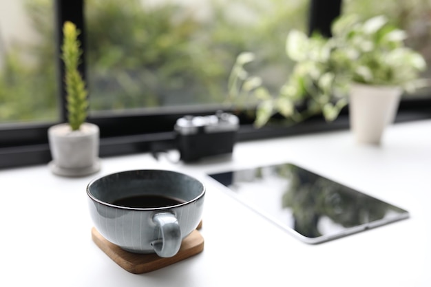 Blue coffee cup and tablet and plants on wooden table in front of window