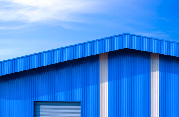 Blue corrugated metal warehouse with automatic roller shutter door against blue sky background