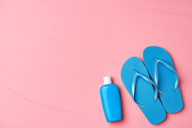 Blue cosmetic bottle with sunscreen cream and flip-flops on pink background