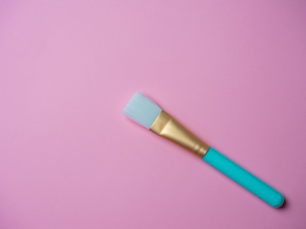 A blue cosmetic brush for applying face masks lies on a pink background. Cosmetic accessories. Top view, flat lay