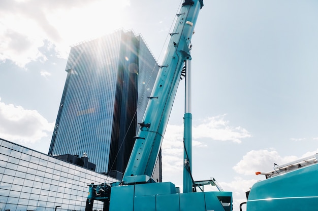 Blue crane lifting mechanism with hooks near the glass modern building,