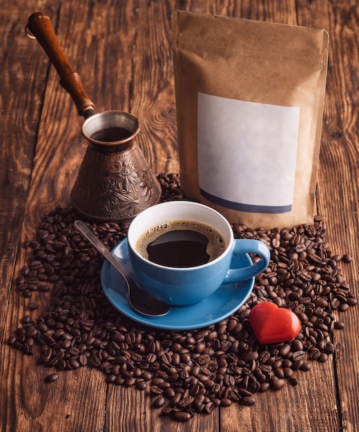 Blue cup of coffee, beans, turkish coffee pot, and craft paper pouch bag on wooden background