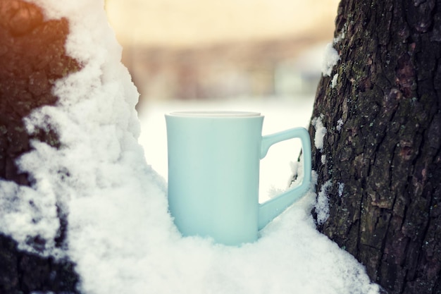 Blue cup of tea stands in snow on the tree branches